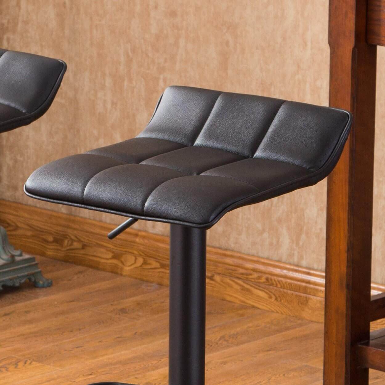 Black cushioned swivel bar stool with bonded leather seat in a dining room setting