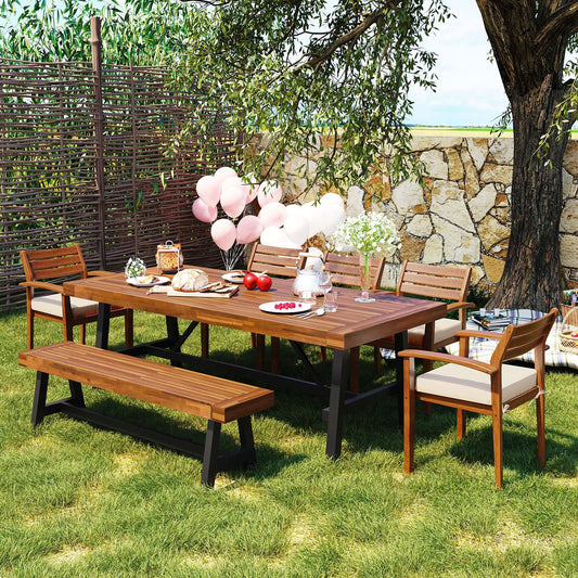 Outdoor wood dining set for 7-8 people in a garden setting with benches, chairs with removable cushions, and a thicker table adorned with food.