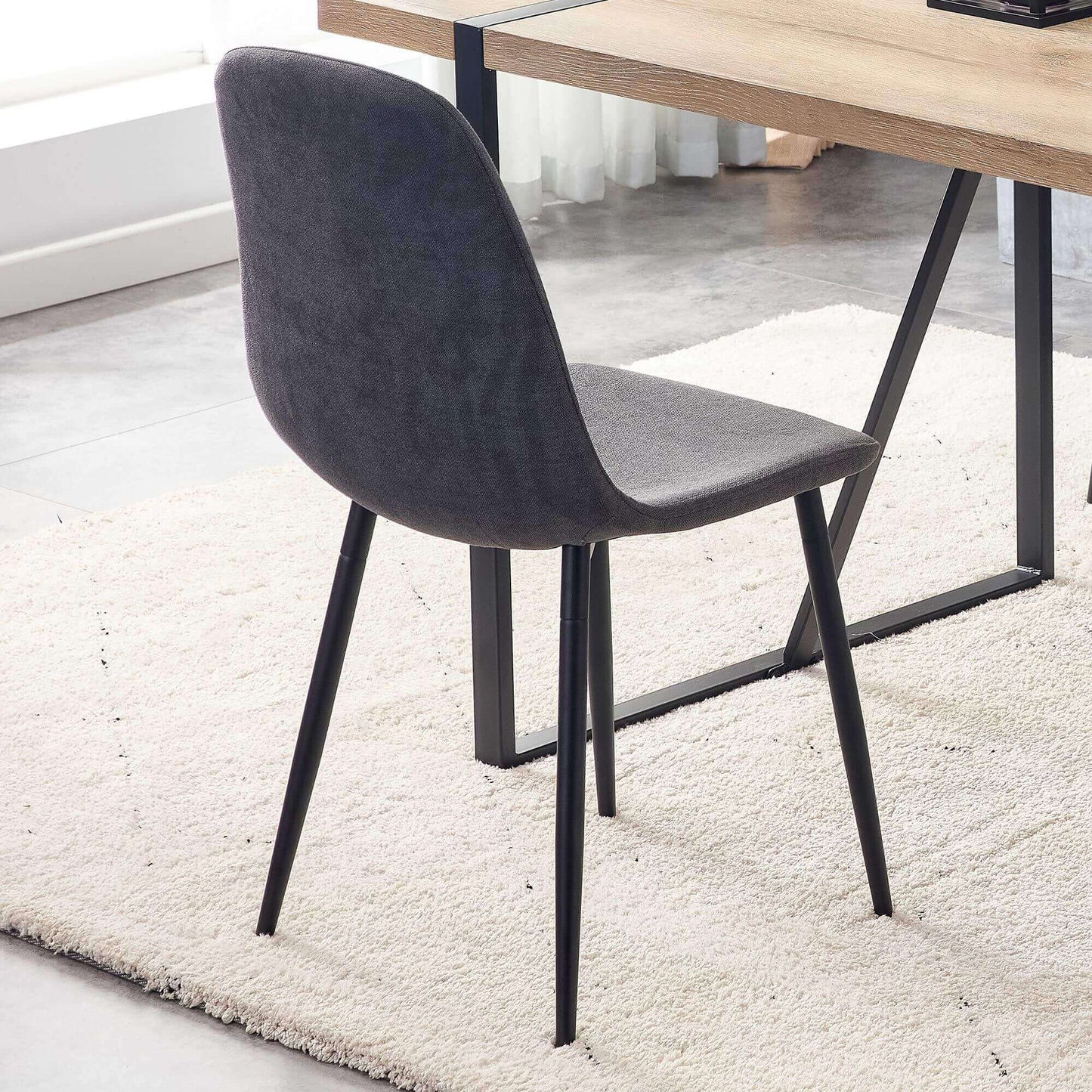 Modern medieval style dark gray chair with metal legs in a bright room with a wooden table and a light rug